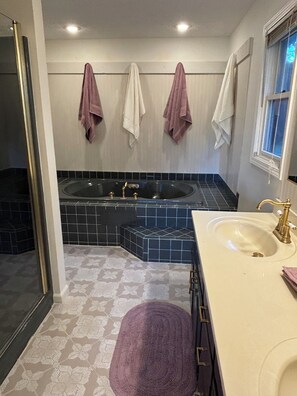 Un baño con bañera, lavamanos y tres toallas colgadas en la pared.
