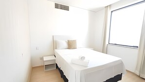 Ein schlicht eingerichtetes Schlafzimmer mit einem Einzelbett, einem kleinen Nachttisch und einem Fenster, das für natürliches Licht sorgt.
