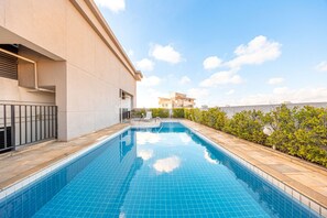 A swimming pool with a tiled edge, a metal railing, and a view of a building in the background. - Apartment with 1 parking space near Alphaville | 1602 (Osasco)
