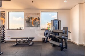 Een sportschool met trainingsapparatuur, een bank en grote ramen met uitzicht over de stad.