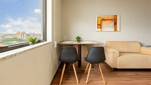 A modern living room with a view of a cityscape, a dining area with two chairs, a table, and a sofa.