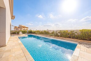 A swimming pool with tiled edges, a stone deck, and a view of buildings in the background. - Hospedez - Spacious apartment w/cupboard ap1701 (Osasco)