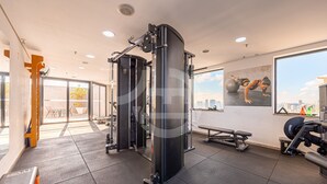 A gym with exercise equipment, a large window, and a view of the city. - Apartment with 1 parking space | UN1604 (Osasco)