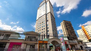 A multi-story building with a modern architectural design, featuring a prominent entrance with a glass canopy and a sign for a business establishment. - Apartment with 1 parking space | UN1604 (Osasco)
