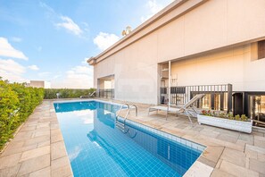 A swimming pool with a tiled deck, a metal ladder, and a planter with plants. - Hospedez - Spacious apartment with kitchen 1306 (Osasco)