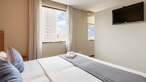 Hotellihuone, jossa on sänky, seinälle asennettu taulutelevisio ja ikkuna, josta avautuu näkymä kaupunkiin.