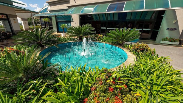 Een hotel binnenplaats met een fontein in het midden, omringd door weelderig groen en een overdekt terras.