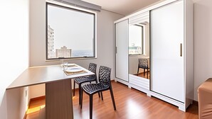 A modern, compact living space with a dining area, a large window offering a city view, and a sliding closet door. - Apartment with kitchenette - includes 1 parking space - UN1309 (Osasco)