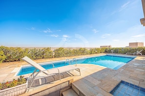 A rectangular swimming pool with a clear blue water, surrounded by a tiled deck, and a lounge chair.