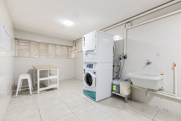 A laundry room with a washing machine, a sink, and a stool.
