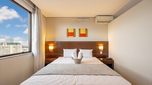 Een hotelkamer met een groot bed, twee wandlampen, een raam met gordijnen en uitzicht op de stad.