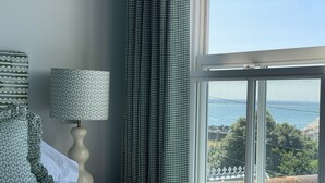 A bedroom with a bed, a lamp, and a view of the sea through a window.