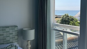 A bedroom with a bed, a lamp, and a window with a view of the sea.