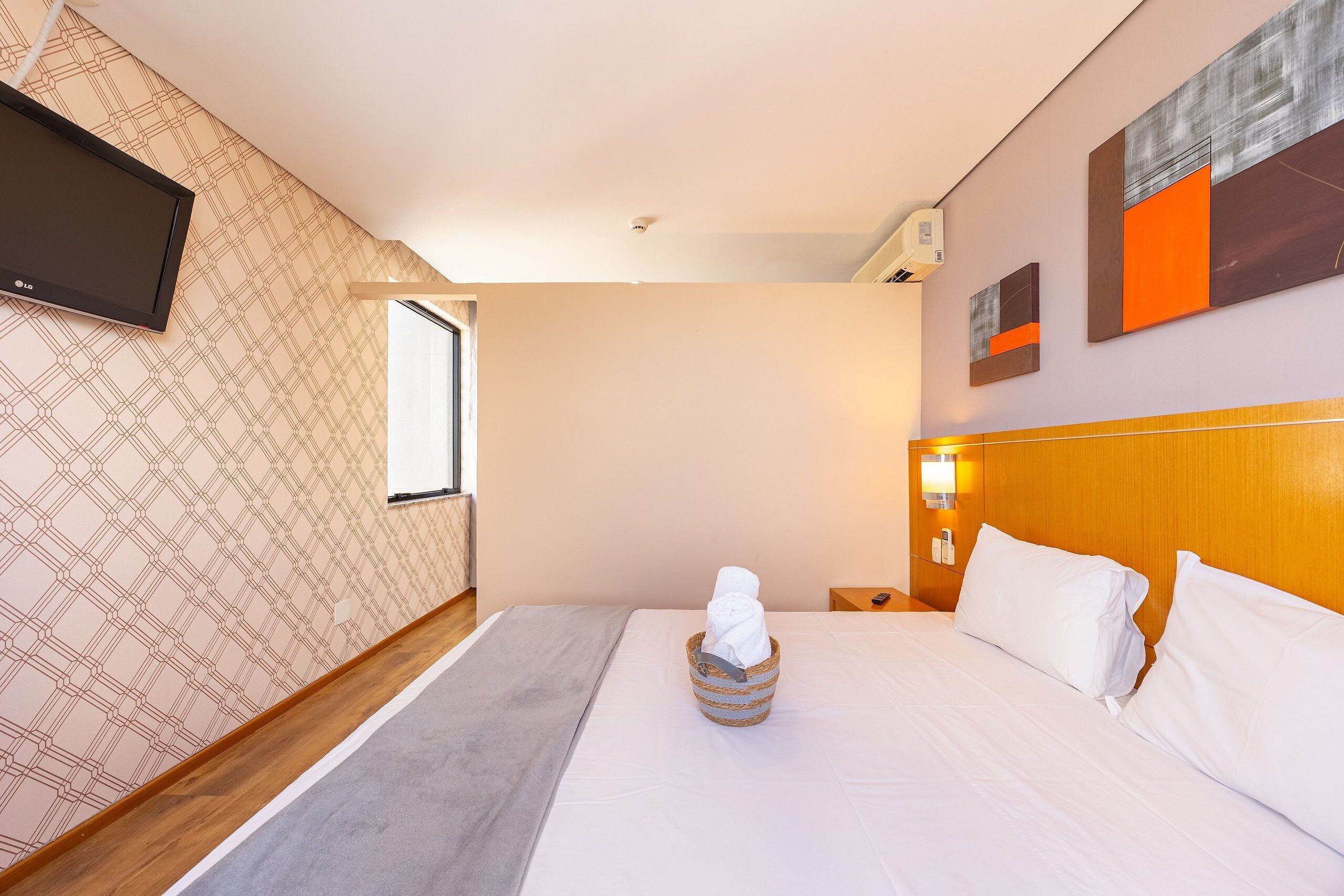A hotel room with a bed, a TV mounted on the wall, a window, and artwork on the wall.