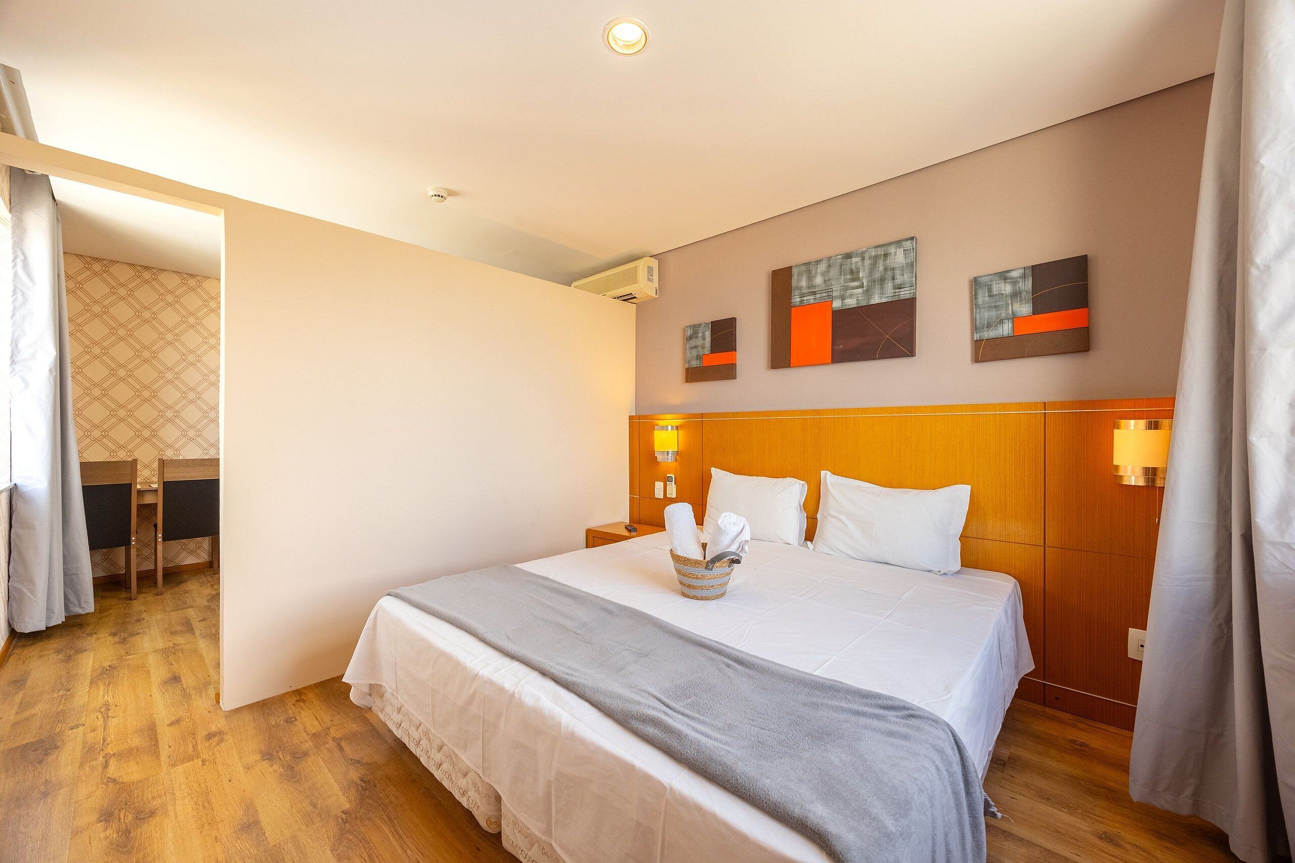 Une chambre d’hôtel avec un grand lit, une tête de lit en bois et une petite table sur laquelle se trouve un panier à serviettes.