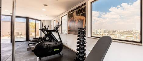 A gym with exercise equipment, large windows, and a city view.