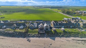 Un hotel costero con edificios de piedra, una playa de arena y un extenso campo verde al fondo.