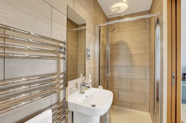 Un baño moderno con ducha de vidrio, un lavabo blanco con grifo cromado y un perchero para toallas.