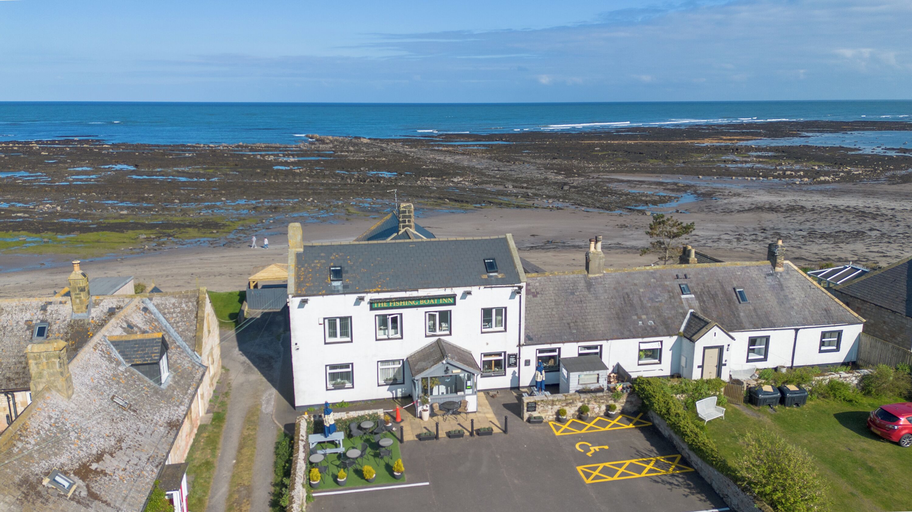 Ein Küstenhaus mit dem Schild "The Fishing Boat Inn", einem Parkplatz und Blick auf das Meer.