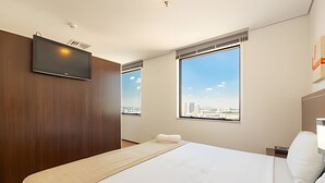 A hotel room with a large bed, a TV mounted on the wall, and a city view through the windows. - Hospedez - Beautiful apartment near Alphaville ap1505 (Osasco)