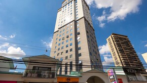A tall building with multiple floors and numerous windows, surrounded by other buildings and power lines. - Hospedez - Beautiful apartment near Alphaville ap1505 (Osasco)