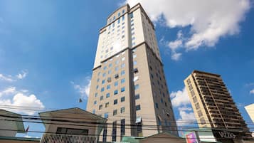 Um edifício alto com vários andares e inúmeras janelas, cercado por outros edifícios e linhas de energia.