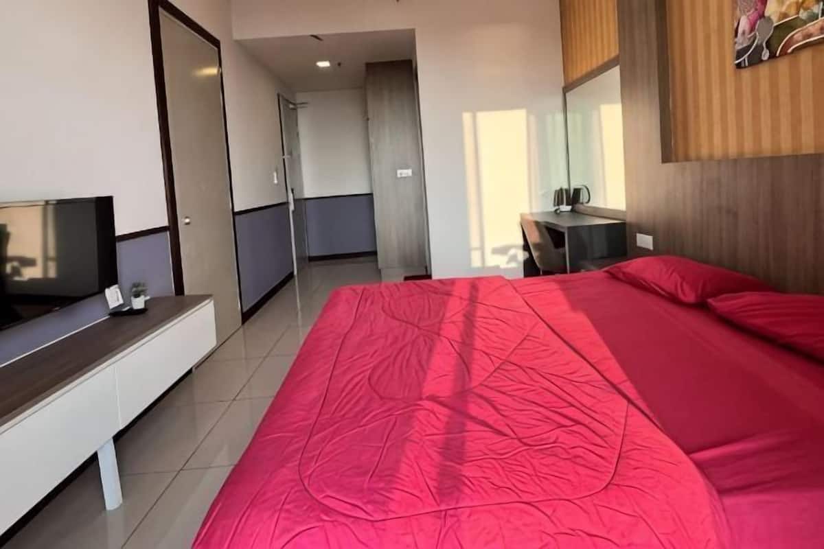 A hotel room with a large bed, a TV on a stand, a desk with a chair, and a door leading to a bathroom.
