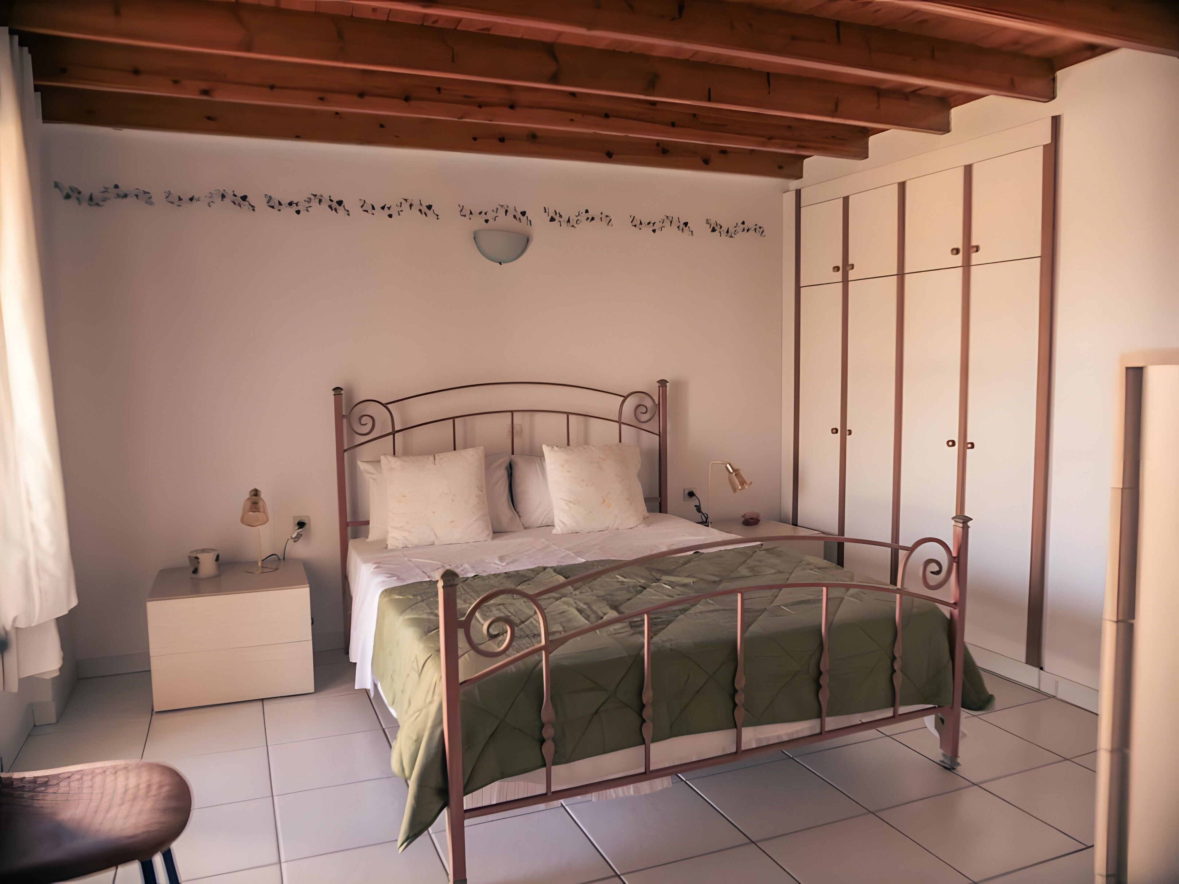 A bedroom with a metal bed frame, a green bedspread, a bedside table with a lamp, and a wall-mounted light fixture.