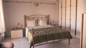 Une chambre à coucher avec un cadre de lit en métal, une couvre-lit verte, une table de chevet avec une lampe et un luminaire fixé au mur.