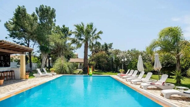 Une piscine entourée d’arbres et d’un bâtiment, avec des chaises longues et des parasols.