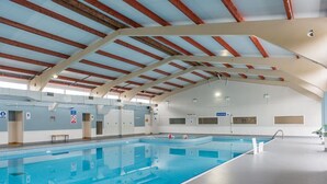 Une piscine intérieure dotée d’un haut plafond, de poutres apparentes et d’un espace de baignade dégagé.