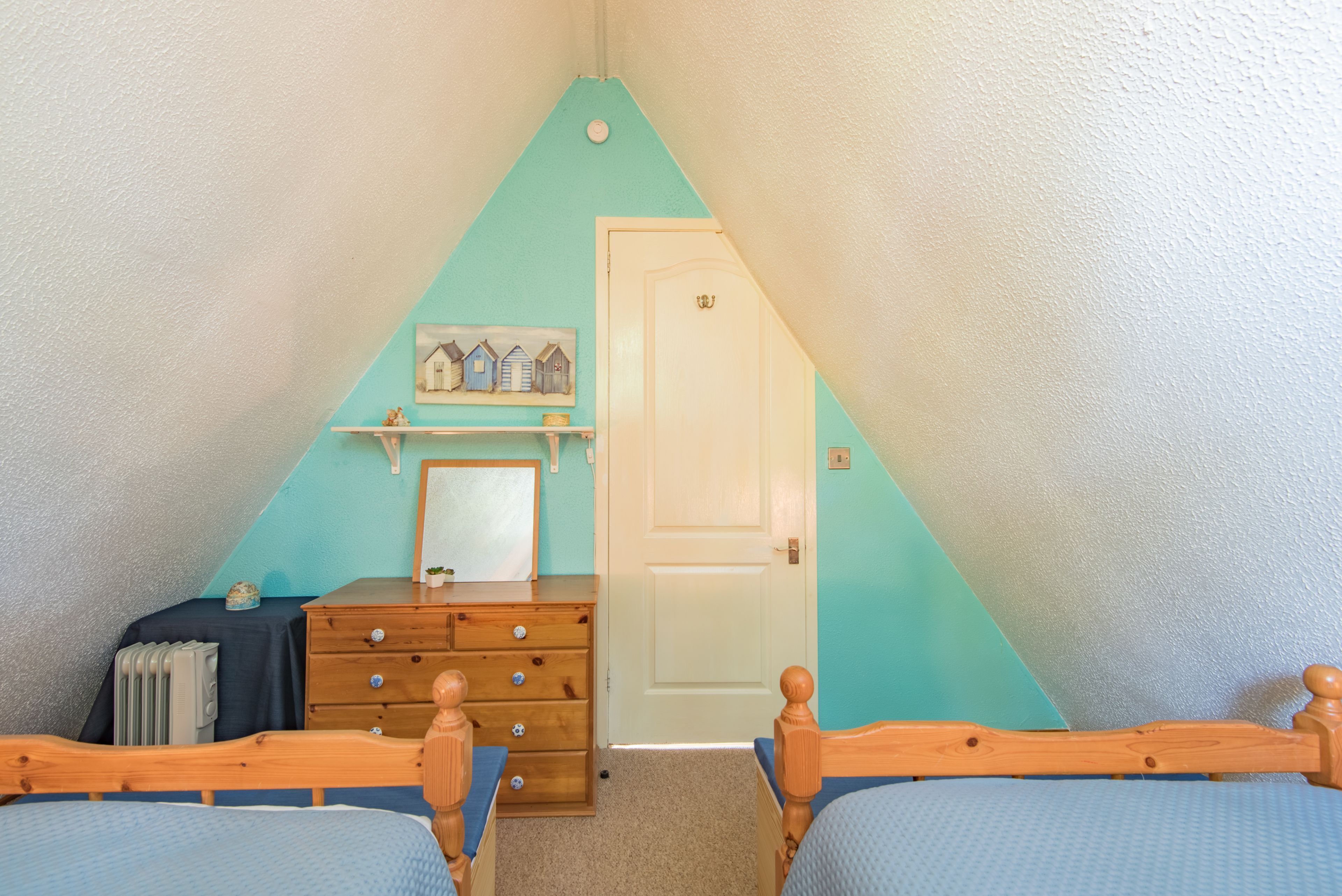 Een slaapkamer met twee houten bedden, een kapstok, een radiator en een deur.