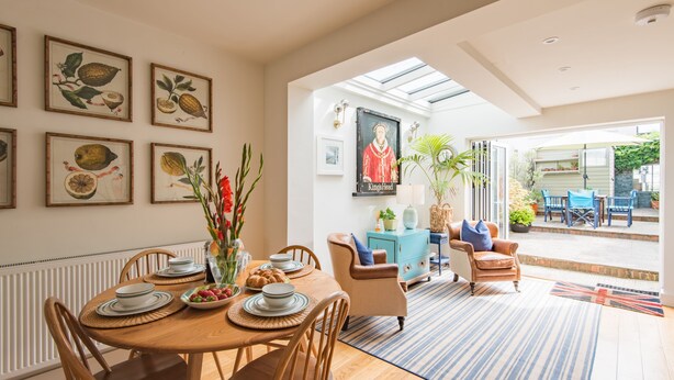A dining area with a round table, chairs, and a vase of flowers. There are framed botanical prints on the wall. - Wisteria Cottage, Deal (Deal)