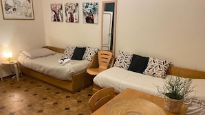 A hotel room with two beds, a wooden table, a chair, a lamp, and wall art.