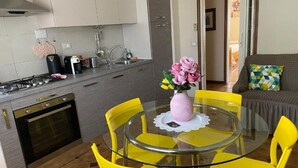 A modern kitchen with a gas stove, oven, and a dining area with a glass table and yellow chairs.
