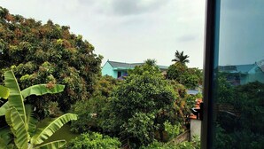 Vista desde una ventana con un jardín exuberante y una escalera de piedra que conduce a un edificio con techo azul.
