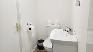 Un baño pequeño y blanco con inodoro, lavamanos y dos rollos de papel higiénico en la pared.