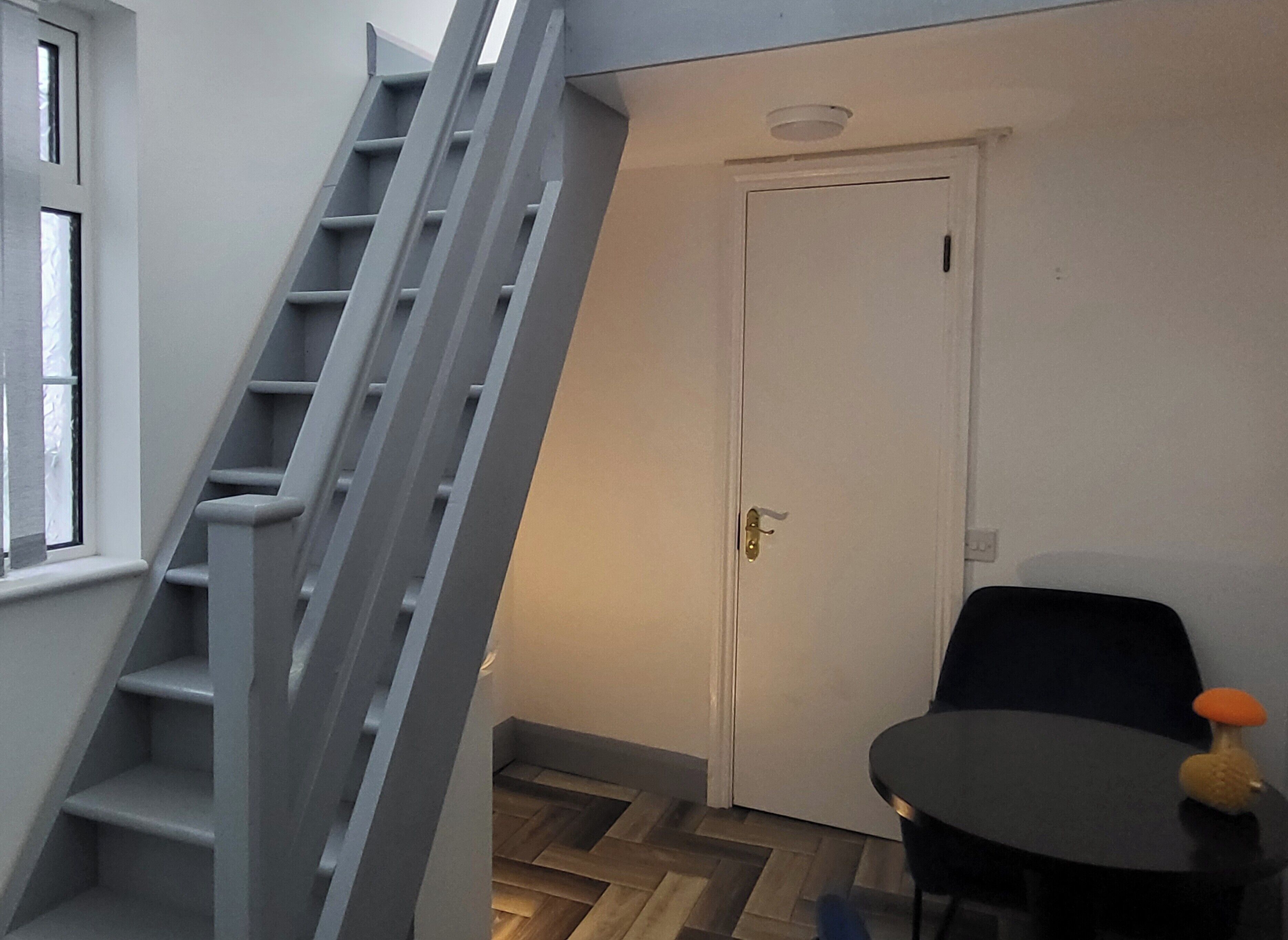 A staircase leading to a landing, a white door, and a small table with a chair.