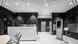 Una zona d'entrada amb un disseny modern, que destaca un taulell d'informació amb la inscripció "BLISKA WOLA TOWER", parets de marbre i un sostre amb un disseny geomètric únic.