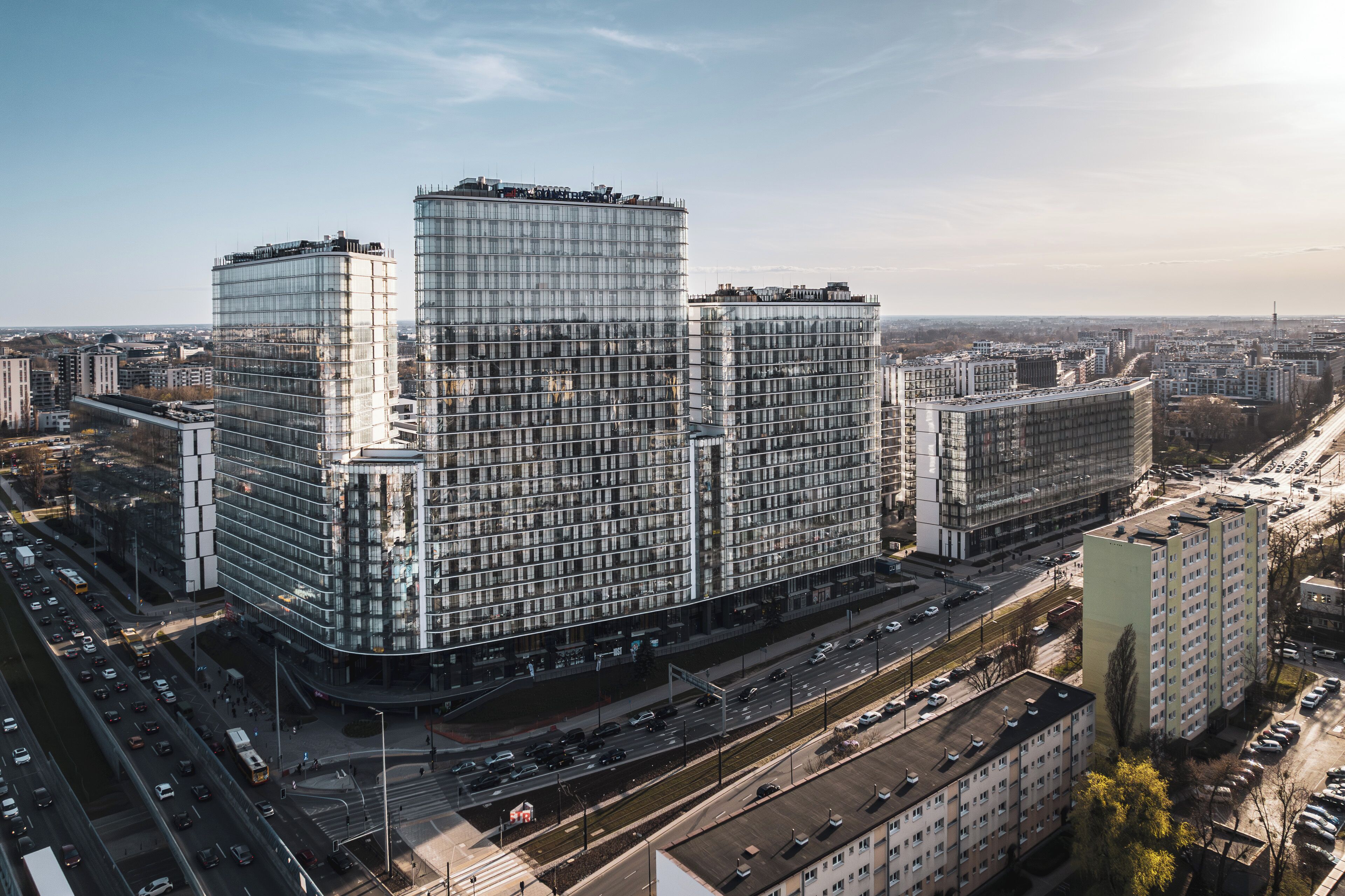 A modern high-rise building with a glass facade, surrounded by a busy urban environment with multiple roads and other buildings.