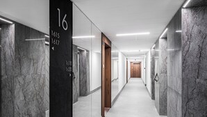 Passadís modern amb parets de marbre, portes numerades i una porta de fusta al final.