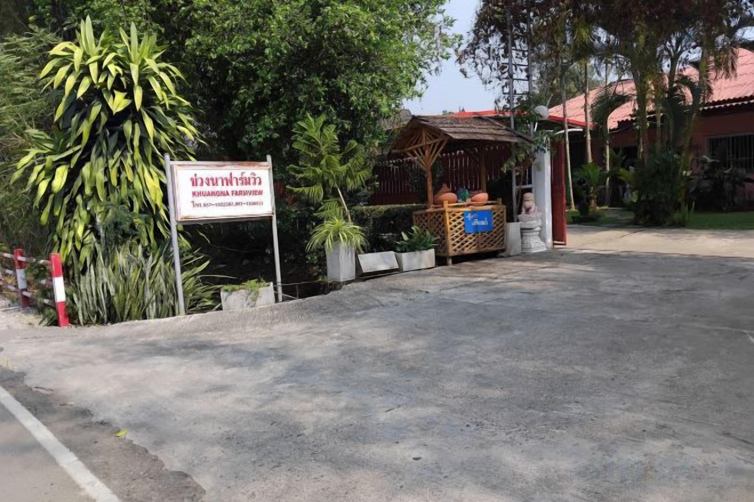 A gated entrance with a sign, a covered seating area, and a building with a red roof in the background.