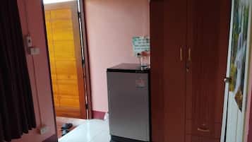 Una habitación con un armario de madera, un refrigerador pequeño y una puerta que da a otra habitación.