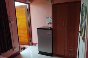 A room with a wooden wardrobe, a small refrigerator, and a door leading to another room. - Khuang Na Farmview (Mae Chaem)
