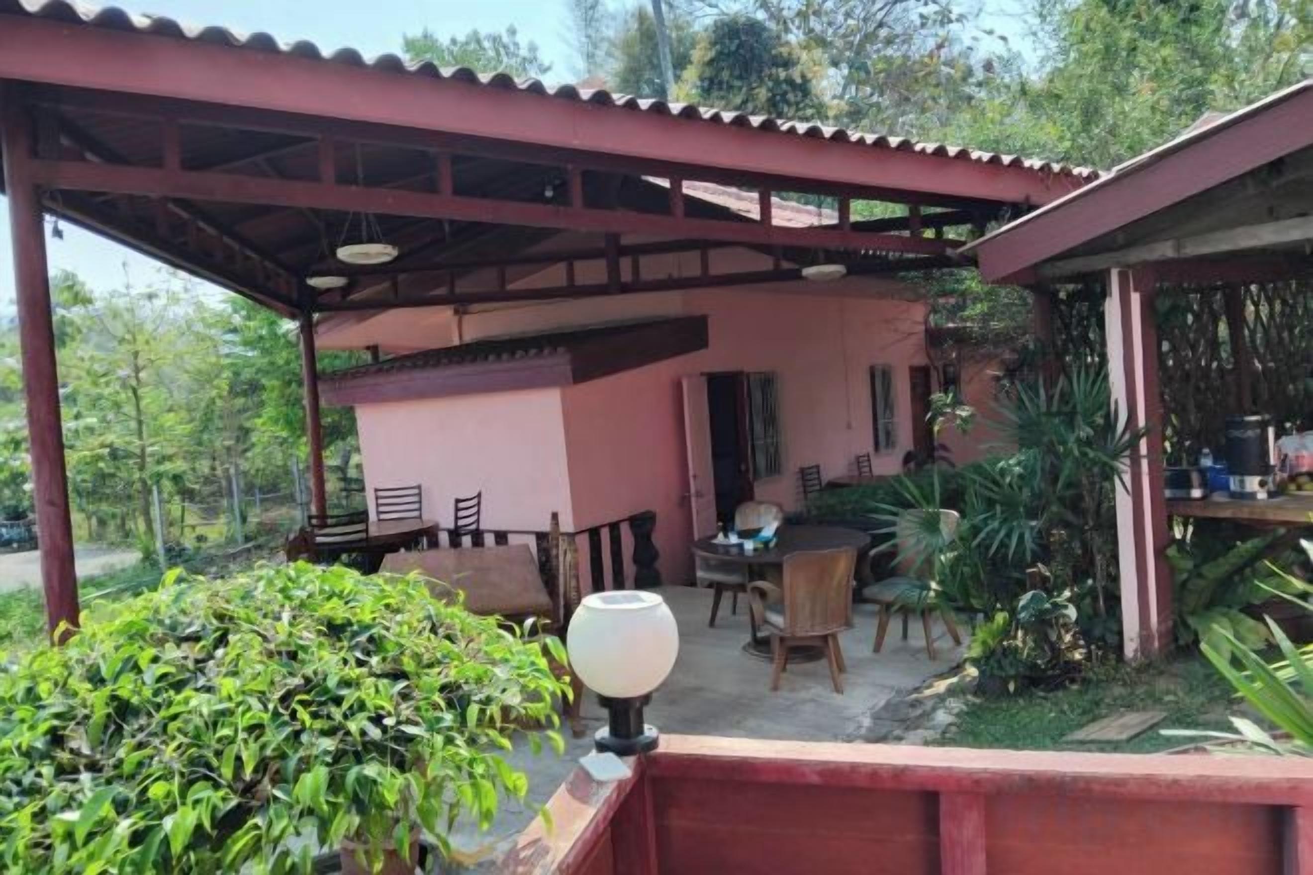 Un espacio exterior techado con una mesa y sillas, rodeado de follaje.