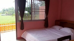 A single bed with a wooden headboard, a small wooden table, and a window with curtains. - Khuang Na Farmview (Mae Chaem)
