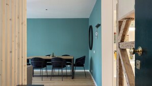 Une pièce aux murs de couleur turquoise, avec un plancher en bois, une table à manger entourée de chaises et une porte au design rustique.