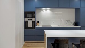 Une cuisine moderne avec des meubles bleus, un four Bosch, un plan de travail blanc et un coin repas avec deux chaises.