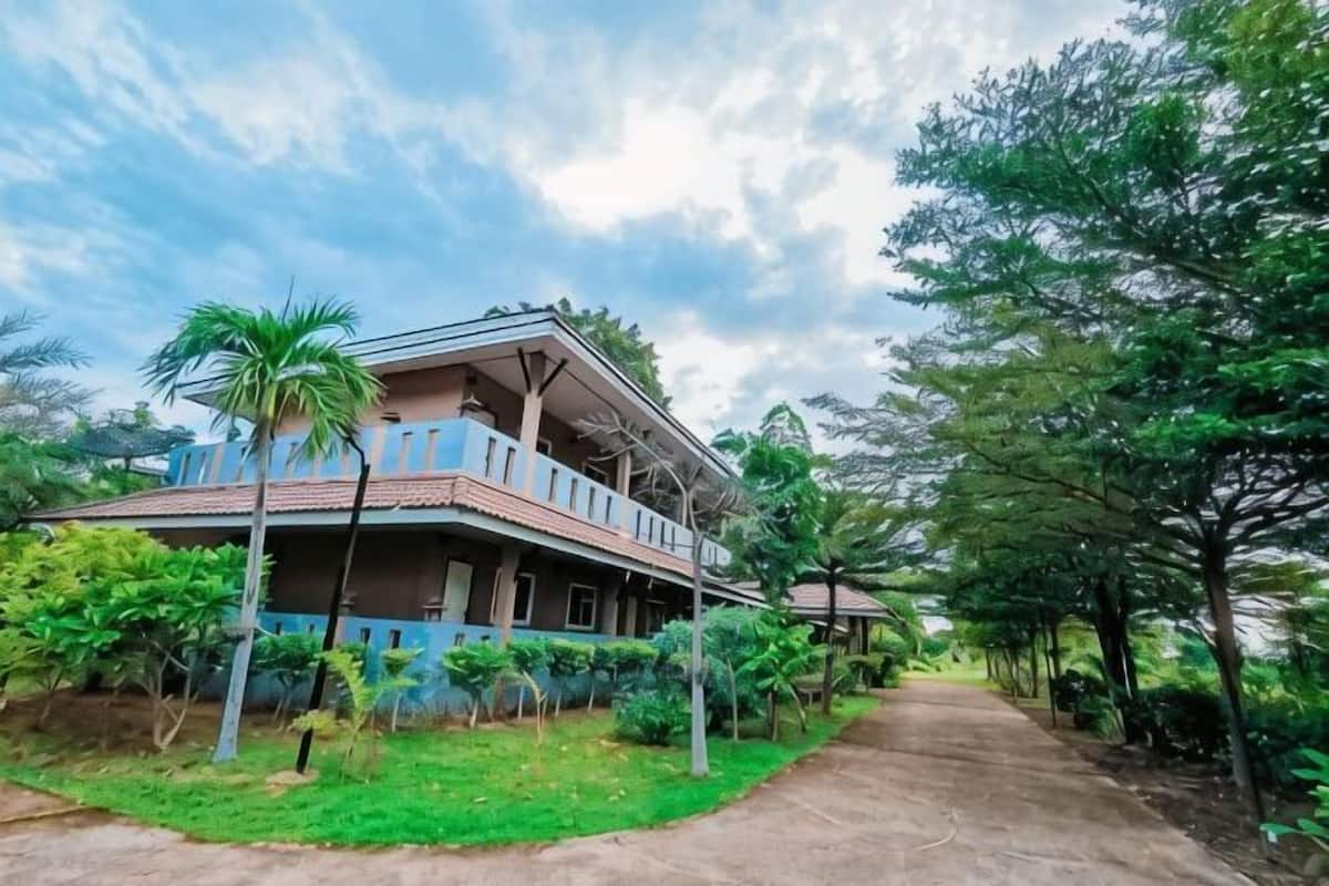 A two-story building with a balcony, surrounded by greenery and a pathway.