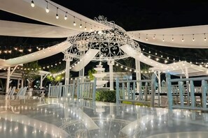 Een buitengebied met een glanzende vloer, een witte structuur als een gazebo en lichtslingers.